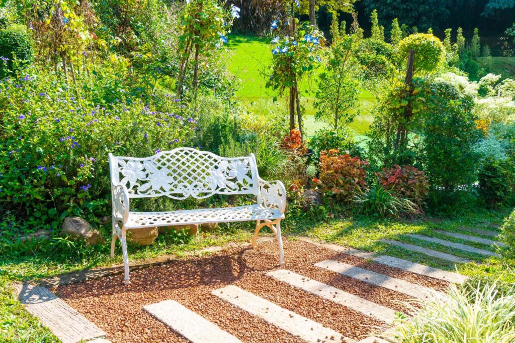 Nostalgische Gartenbank in einem herrlichen Bauerngarten mit einem Gartenweg aus Holzschwellen