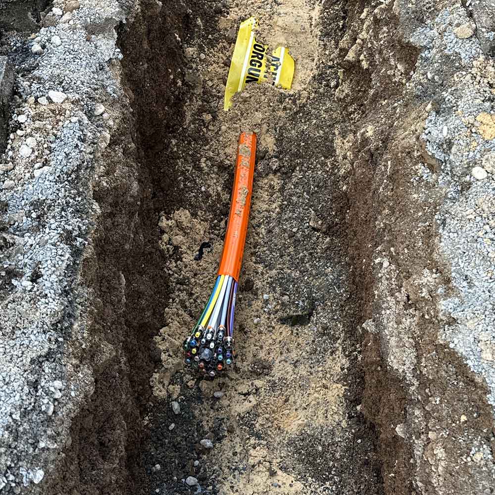 Blick in eine Straße mit einem Glasfaser-Kabel, aus dem ein Bündel bunter Einzelkabel hervorschaut