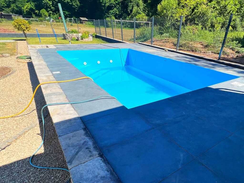 Poolbau eines kleinen blauen Pools in einem Podest mit Terrasse, Mauer und Stufen zum Pool in einem angelegten Garten mit Zaun
