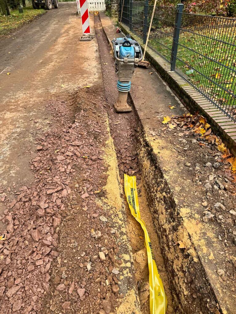 Wacker steht in einem bereits verdichteten und halb zugeschütteten Graben einer Glasfaser-Verlegung