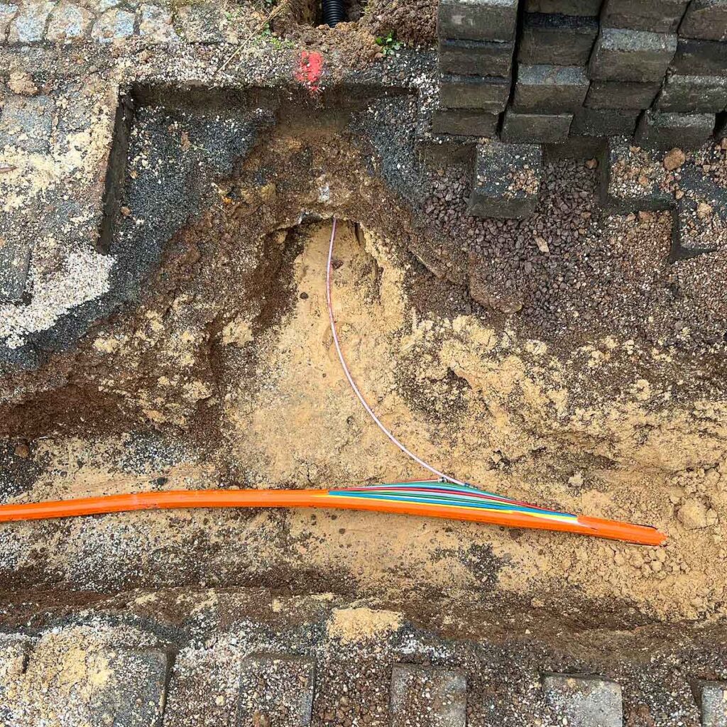Orangenes Glasfaser Kabel im Bode, bunte einzelne Kabel sind sichtbar, eines führt in ein Kabelrohr