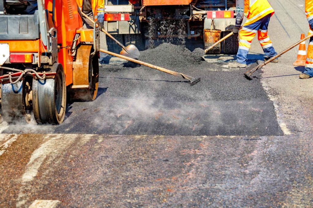 Teeren einer Straße: viel Mitarbeiter verteilen den heißen Teer mit Rechen.