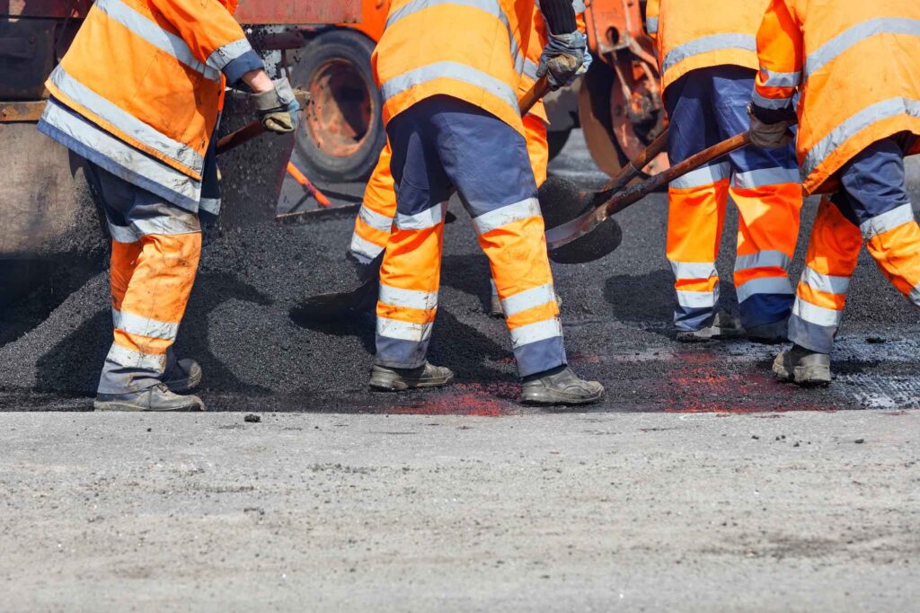 Mitarbeiter arbeiten den frischen Teer in die Straße ein