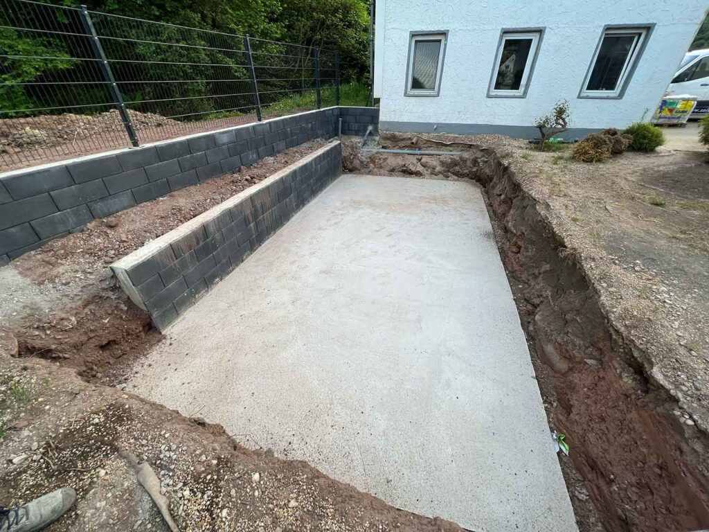Vorbereitung zum Poolbau: Fundament in der ausgehobenen Grube mit einer Einfassungsmauer
