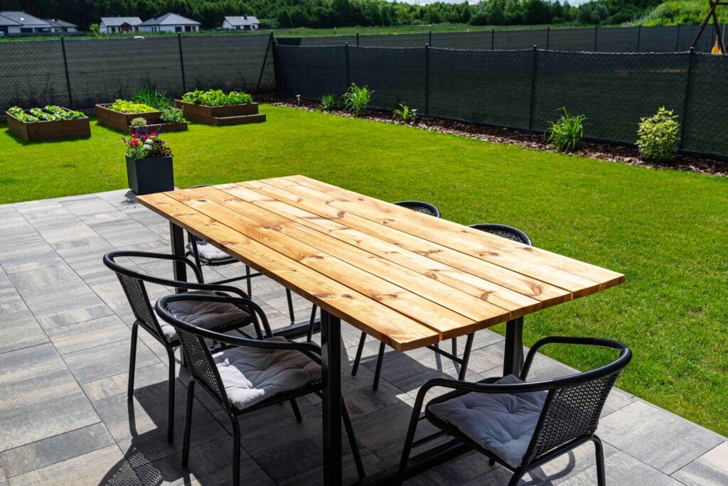 Terrasse mit Hilztisch in einem schön angelegten Garten mit kleinen Hochbeeten und Sichtschutz